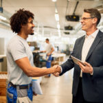 Engenheiro feliz e fornecedor apertando as mãos enquanto cumprimenta no edifício industrial