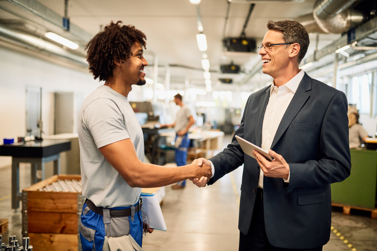 Engenheiro feliz e fornecedor apertando as mãos enquanto cumprimenta no edifício industrial