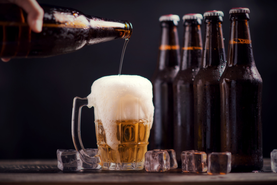 Caneca de cerveja cheio ao lado de garrafas empilhadas em fileiras